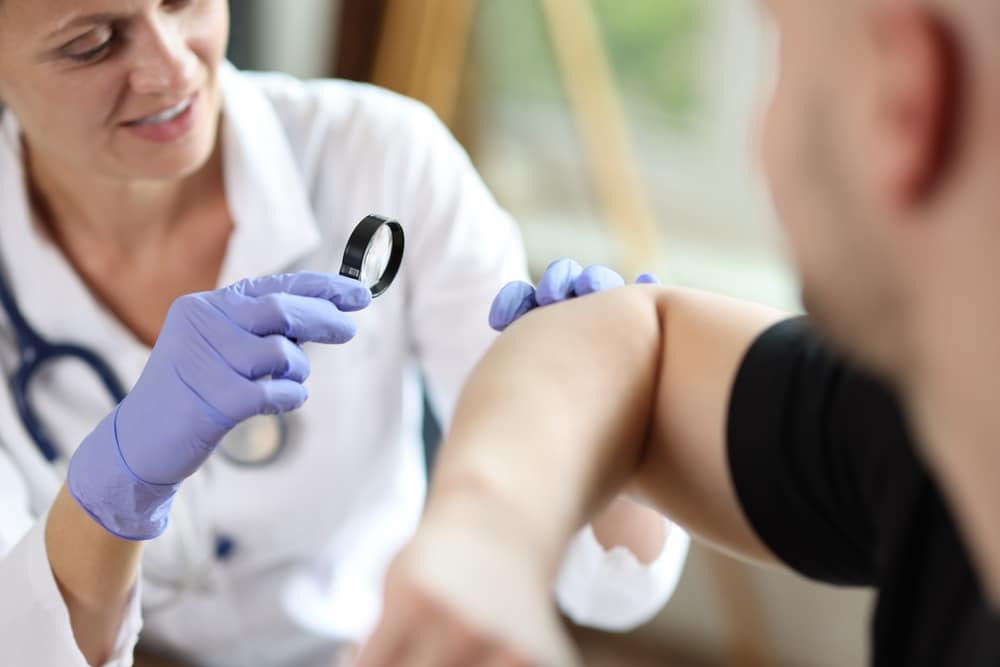 Dermatologist inspecting spot on man’s arm in for preventative dermatology appointment.