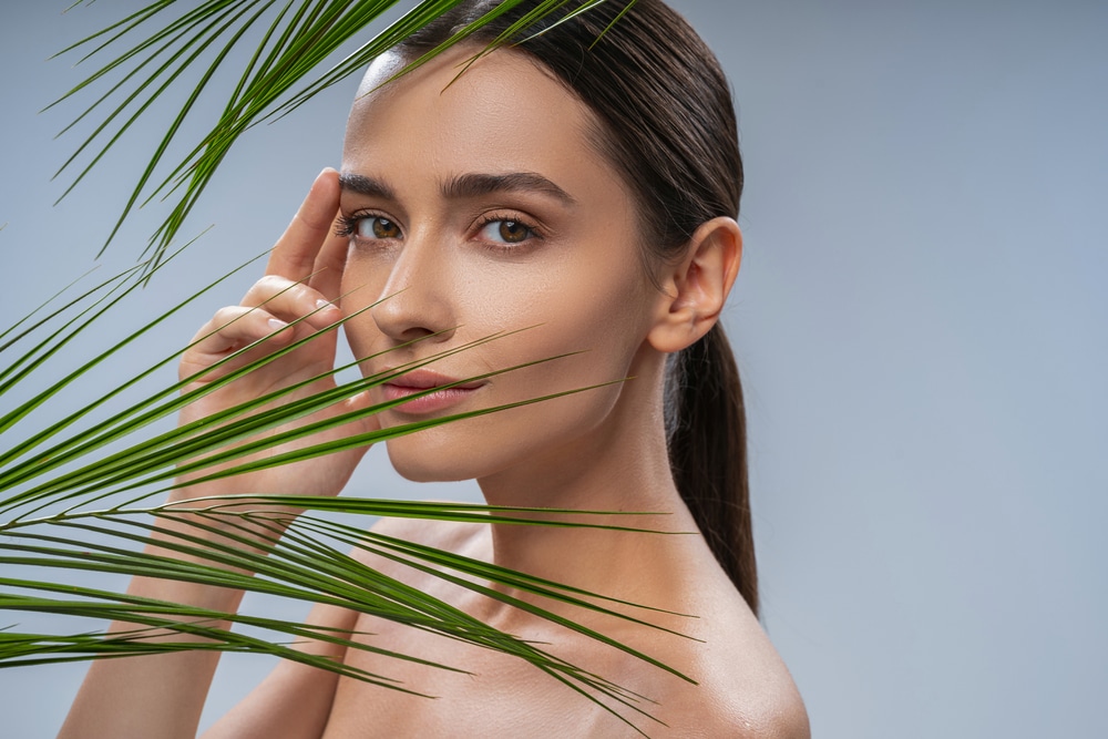 A woman standing behind a palm leaf showing the results of a spring skin refresh in Sarasota