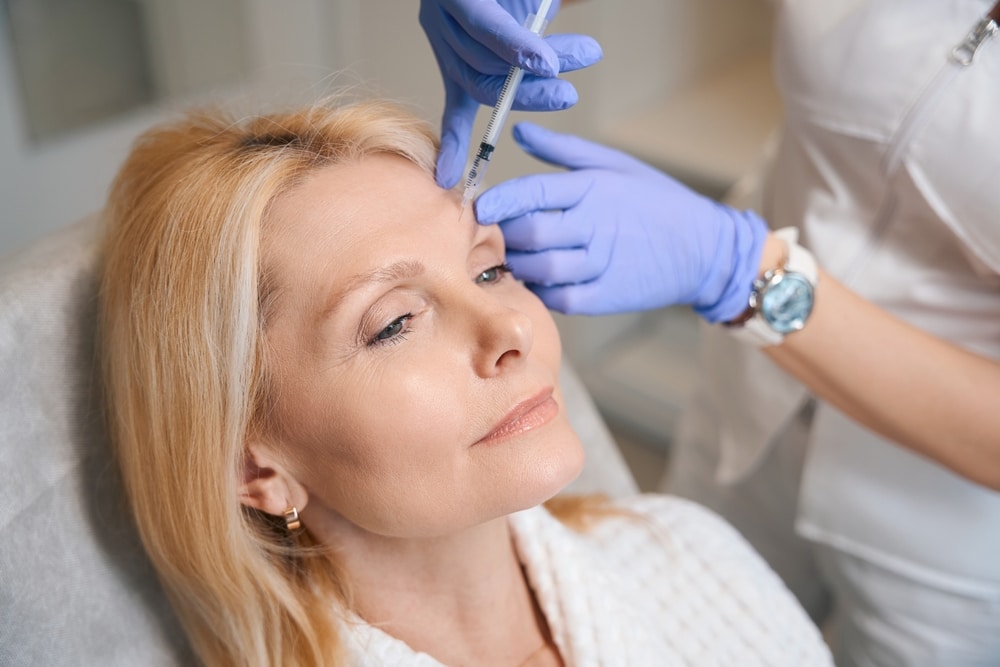 Close-up of woman receiving anti-wrinkle injection from cosmetologist during facial rejuvenation treatment.