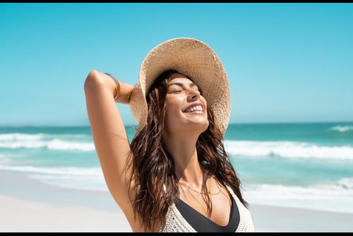Young woman soaks up the sun at the beach, potentially damaging her skin.